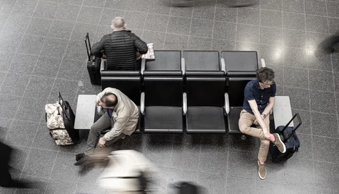 Overhead view of three people sitting on a black bench in a tiled public space.