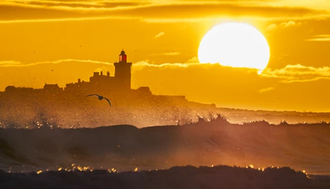 Silhouetted cityscape with cathedral at sunset, large sun behind golden sky and haze.