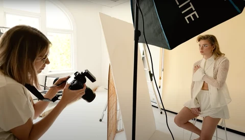 Photographer holding a camera while shooting a model in a studio setting with professional lighting equipment.