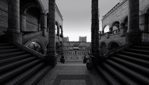 Symmetrical view down a columned corridor toward a distant piazza with classical architecture.