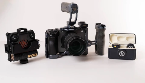 Video production kit with cinema camera, RGB light, wireless microphone, and accessories on white surface.