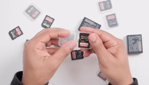 Hands holding SD memory cards with additional cards scattered on white surface.