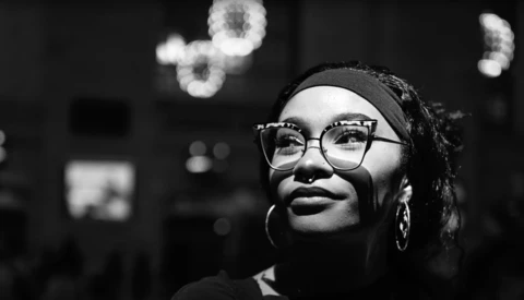 Person wearing glasses and headband looking upward in black and white portrait with bokeh lights in background.