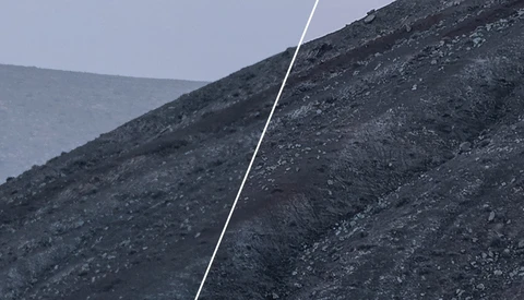 A white rope or cable cutting diagonally across dark, rocky slopes under overcast sky.