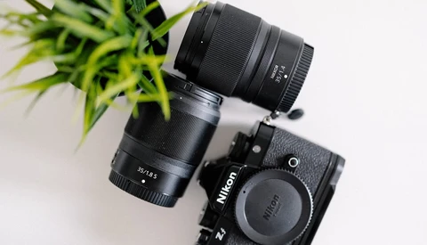 Nikon Z mirrorless camera body with two black lenses and a green plant on white surface.