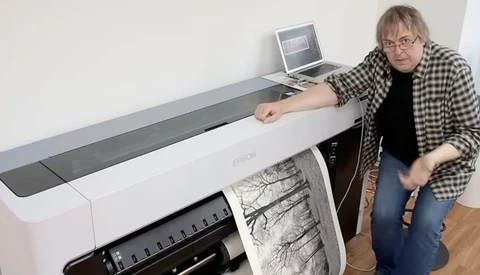 Photographer demonstrating a large-format inkjet printer with a tree branch print output.