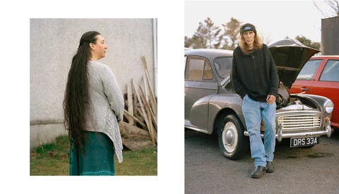 Woman with long dark hair wearing a cream cardigan and teal skirt stands in profile against a white wall.