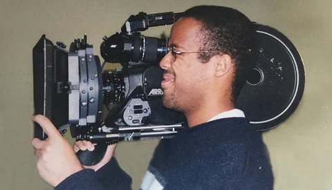 Cinematographer operating a 35mm film camera on his shoulder in profile.