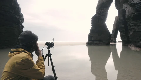Photographer in yellow jacket using tripod to capture dramatic rock formations reflected in still water.