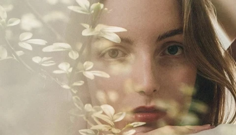 Woman's face partially obscured by delicate white flowers in soft, overexposed lighting.