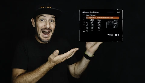 Screenshot of camera dial/wheel settings menu displayed on a smartphone screen held by a man in a black cap.
