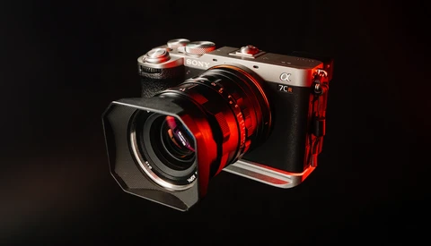 Red and silver mirrorless camera with matching red lens and L-bracket cage against dark background.