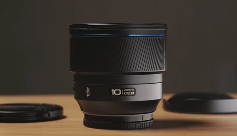 A 10mm prime lens with ribbed rubber grip and metal barrel displayed on wooden surface with soft studio lighting.