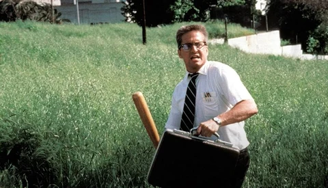 Man in business attire holding a large black briefcase in an overgrown grass field.