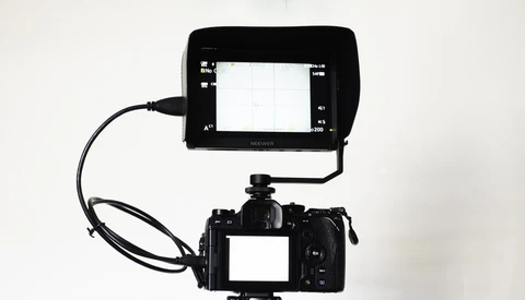 Professional video camera with external monitor mounted on top via cable.