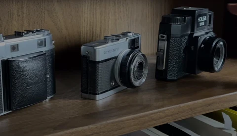 Four vintage rangefinder cameras arranged in a line on a wooden shelf.