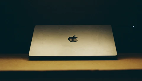 Gold MacBook Pro closed on wooden surface against dark background with dramatic side lighting.