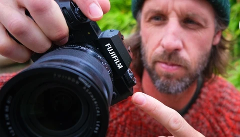 Photographer holding a mirrorless camera with telephoto lens attached, demonstrating proper grip and handling technique outdoors.
