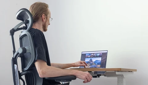 Man in ergonomic office chair working on laptop at desk.