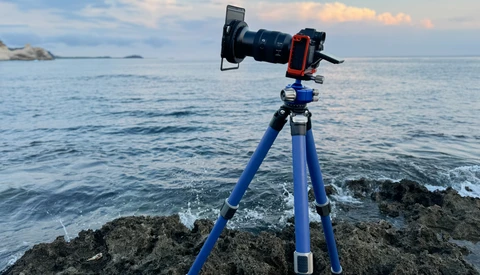 Professional camera on blue tripod mounted on rocky coastline facing calm ocean.