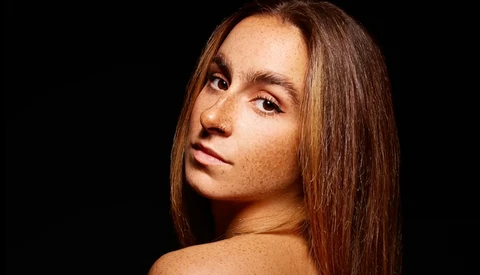 Woman with long brown hair looking over shoulder against black background.