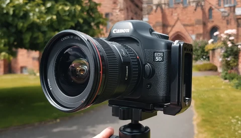Canon EOS 5D Mark IV DSLR with wide-angle lens mounted on tripod, photographed outdoors against brick building.
