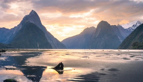 Dramatic fjord landscape with steep mountain peaks reflected in still water at golden hour.