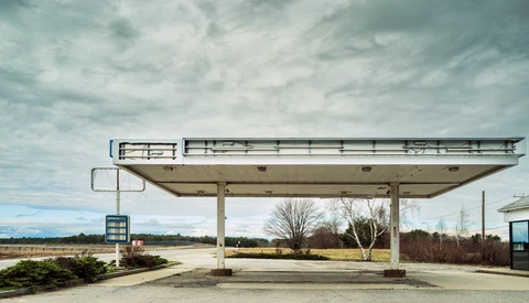 Abandoned gas station canopy with weathered concrete structure under overcast sky.