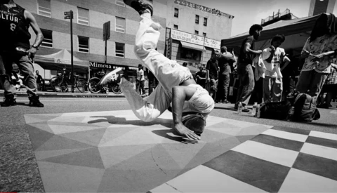 Breakdancer performing a headstand on a checkered street surface during a public performance.