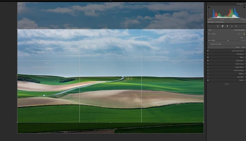 Rolling agricultural landscape with green fields, tan plowed earth, and road, composed using rule of thirds grid overlay.