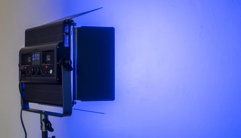 Professional LED panel light mounted on stand with blue gel filter and control panel visible.