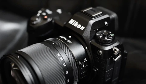 Nikon DSLR camera with attached zoom lens on dark background with secondary camera blurred in background.