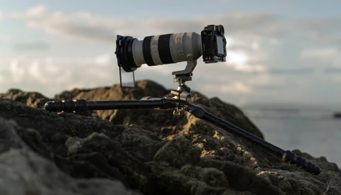 Professional telephoto lens mounted on tripod head positioned on rocky coastal outcrop.