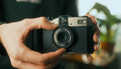 Hands holding a vintage rangefinder camera with textured black body and chrome accents.