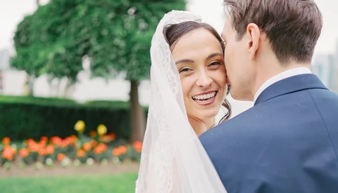 Bride in white veil smiling at groom during outdoor garden wedding ceremony.