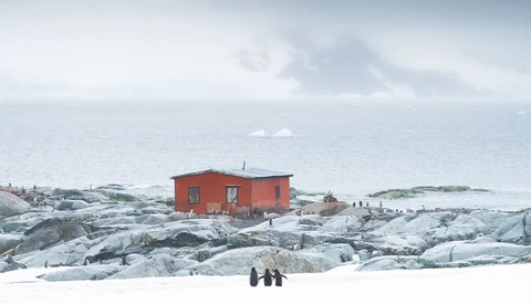 Bright red building on snow-covered rocky terrain with ocean and sky beyond.