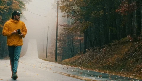 Runner in yellow jacket jogging on misty forest road lined with bare trees and fallen leaves.