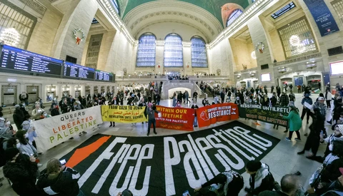 Pro-Palestine demonstration in a grand station with large banners and dozens of participants.