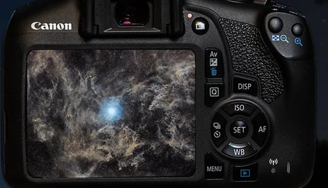Canon DSLR camera displaying a deep space image with nebula and bright star on its rear LCD screen.