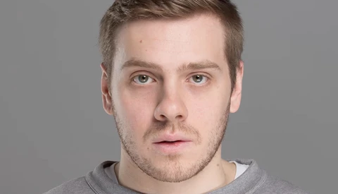 Portrait of a man with short brown hair against a neutral gray background.