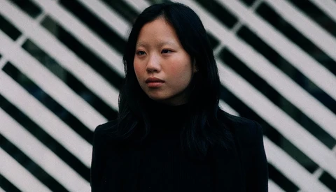 Portrait of a person with long dark hair against a striped geometric background.