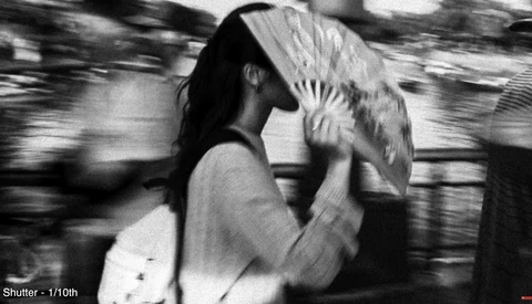 Person in motion holding a fan in front of their face, shot with motion blur and fast shutter speed.