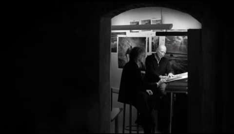 Black and white photograph of two people viewing framed photographs on a gallery wall.