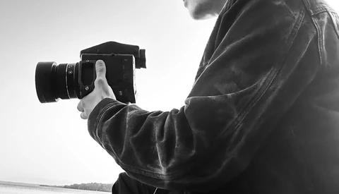 Photographer holding a DSLR camera, shooting from a boat on calm water in black and white.