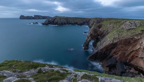 Dramatic coastal cliffs with turquoise water and rocky outcrops under stormy skies.