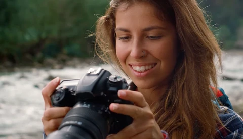 Young woman smiling while holding a DSLR camera with telephoto lens outdoors.