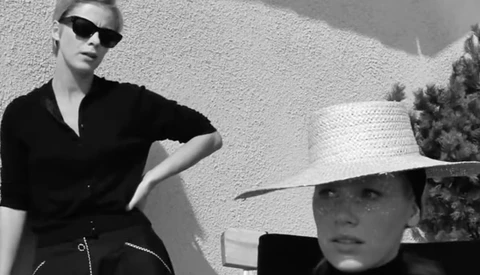 Two figures in sunglasses and dark clothing posed against a textured white wall in stark black and white photography.