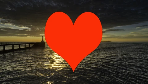 Large red heart shape overlaid on a seascape with a pier and dramatic sunset lighting.