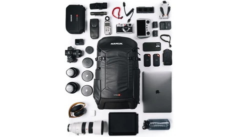 Flat lay of professional photography and videography equipment including camera body, lenses, backpack, laptop, batteries, and audio gear.