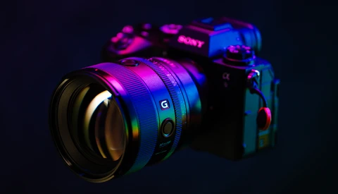 Sony mirrorless camera and lens illuminated with neon magenta and blue lighting against a dark background.